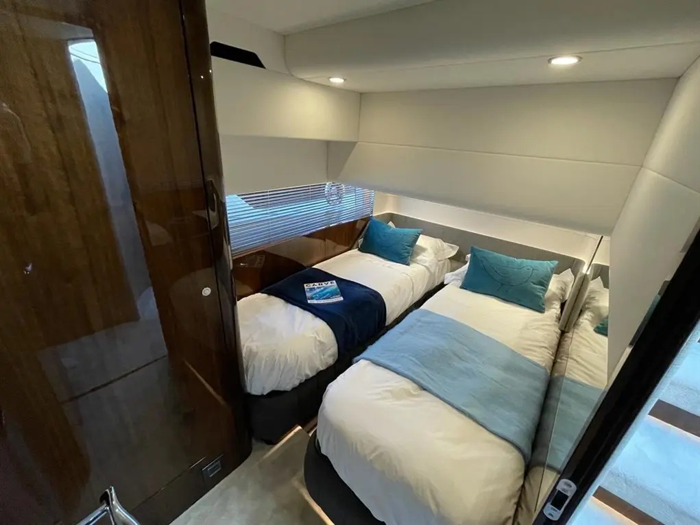 Modern boat cabin with two single beds, light blue throws, and cushions, featuring wooden interiors and ambient lighting.